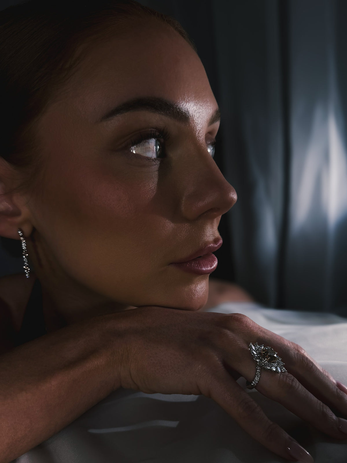 A woman in profile wearing an Australian Chocolate Diamond custom halo ring and Pinnacle diamond earrings